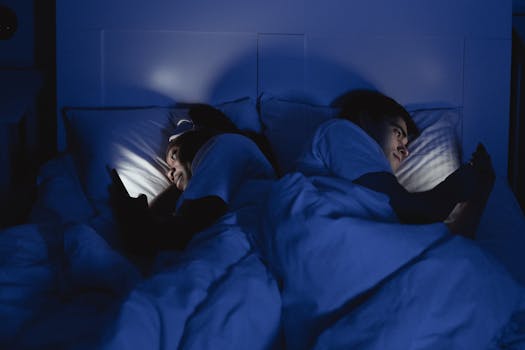 A couple lying in bed using smartphones at night, illuminated by screen light.