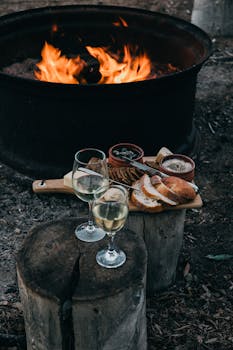 High angle of fire bowl with burning flame and glasses of white wine with snacks on wood stumps