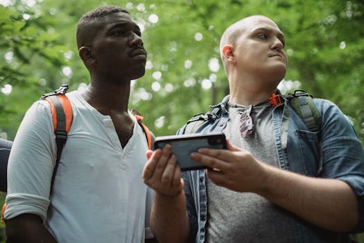 Low angle of focused multiethnic male tourists exploring nature and checking route on mobile phone