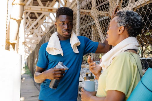 Two adults in sportswear resting outdoors, engaging in lively conversation and rehydration.