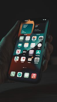 A close-up view of a hand holding a smartphone displaying various app icons, taken at night.